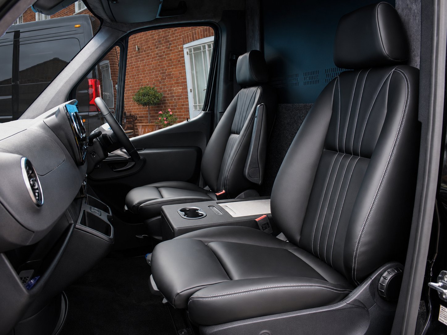 Interior view of a truck cab with black leather seats featuring white stitching and a black steering wheel visible through the windshield