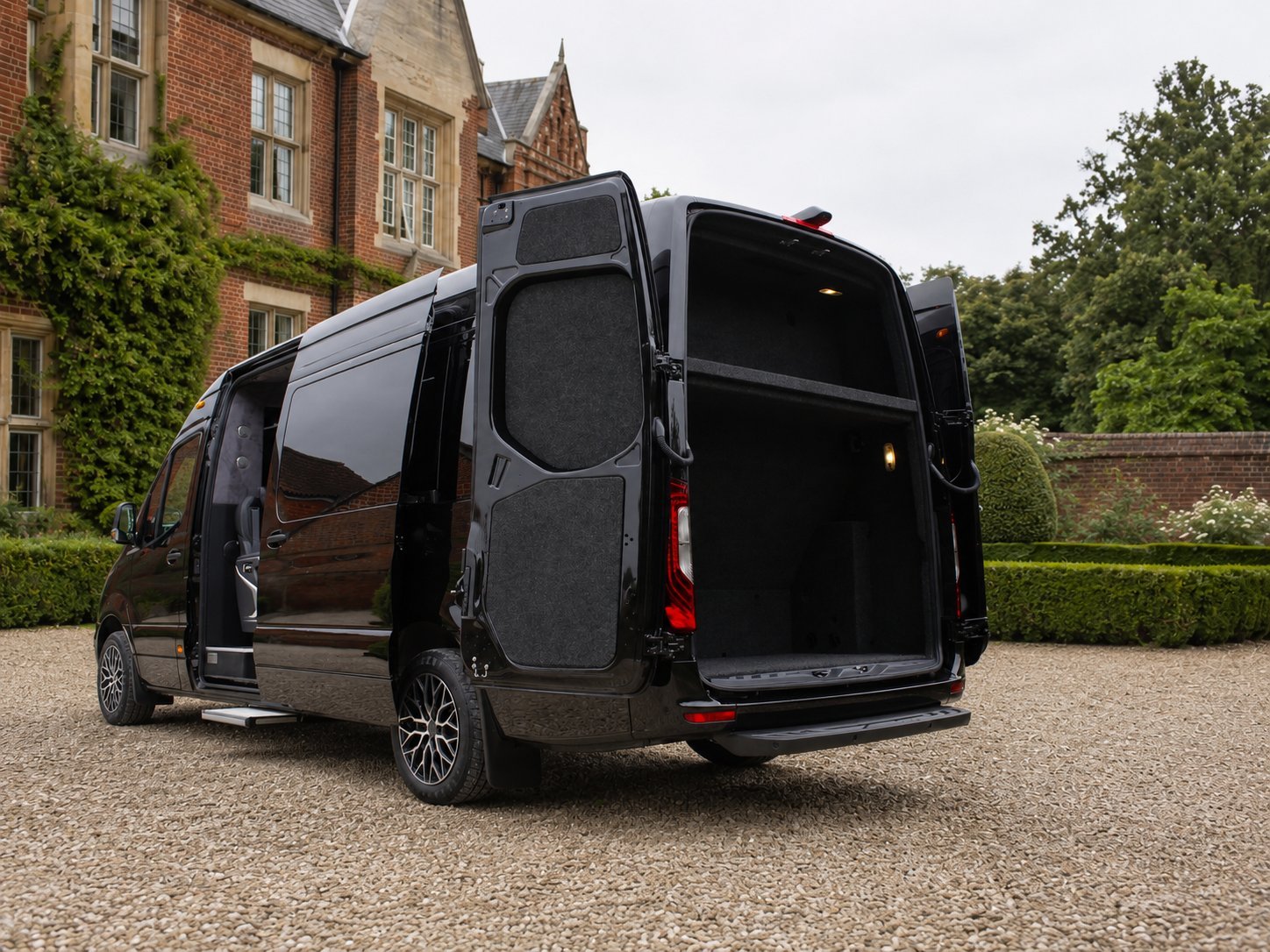 Black commercial van with open rear doors parked in front of a brick mansion with ivy and green hedges